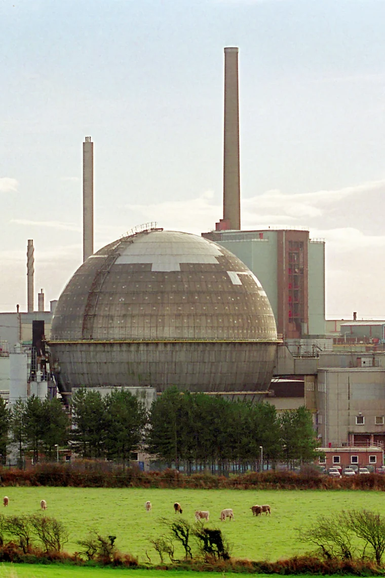 A large domed reactor building and two tall chimneys behind a field