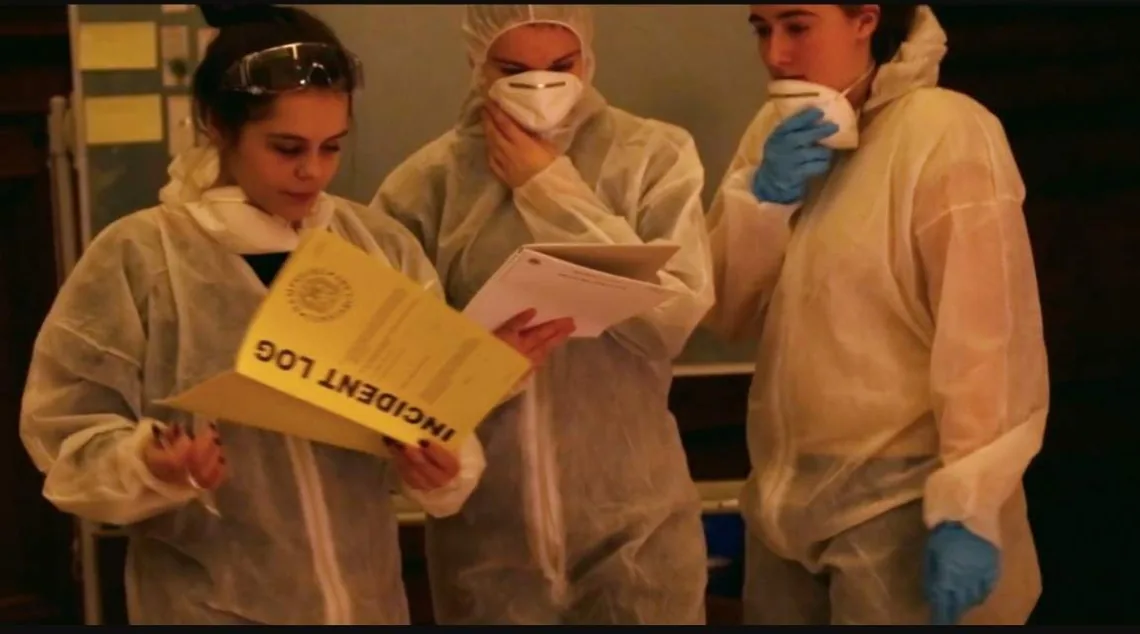 Three people in white forensic suits and face masks read an incident log