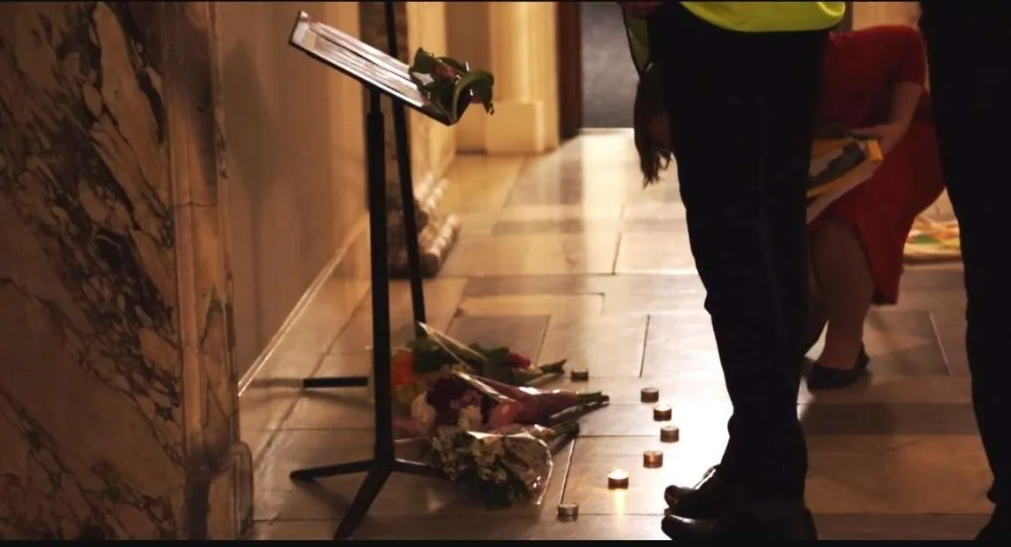 Flowers and tealights on a stone floor beside a music stand, with people standing nearby
