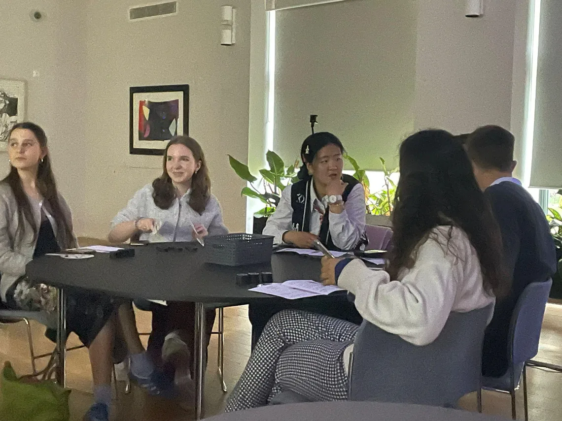 Participants around a table with papers, looking towards the front of the room