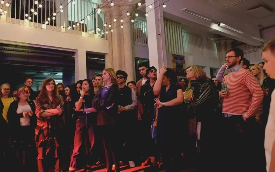 A standing audience in a hall with festoon lights