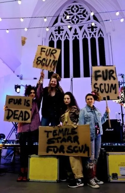 Protesters on a stage holding cardboard placards reading 'Fur scum' and 'Fur is dead'