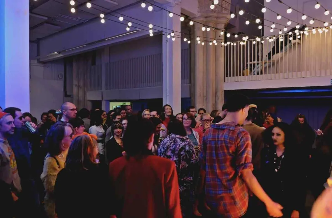 A crowded hall under festoon lights, people standing and talking