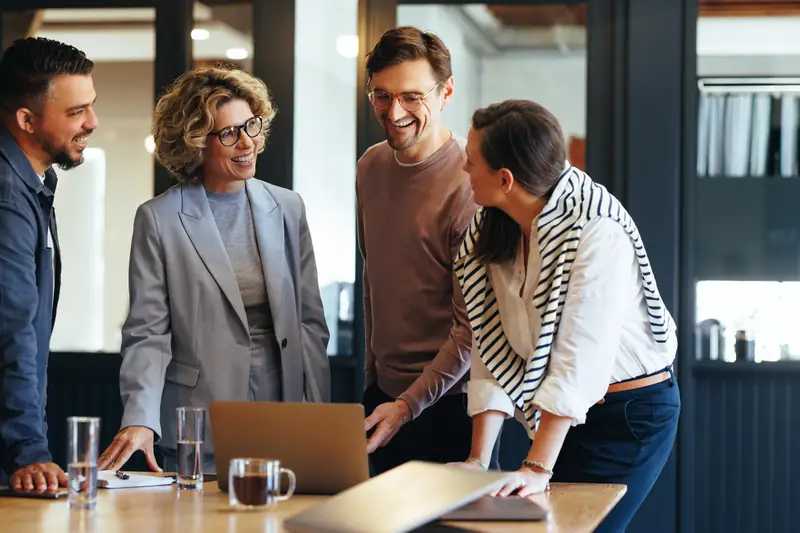 Colleagues laughing together around a laptop