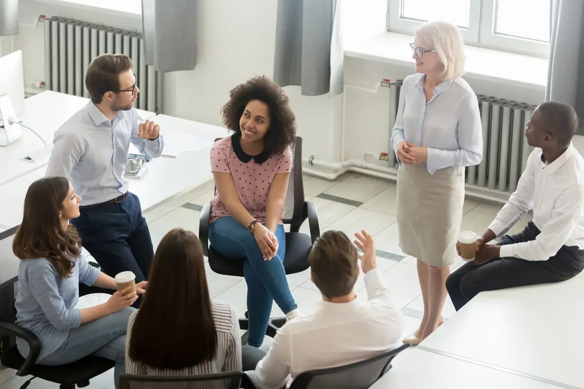 A group seated in a circle, listening to a colleague speak