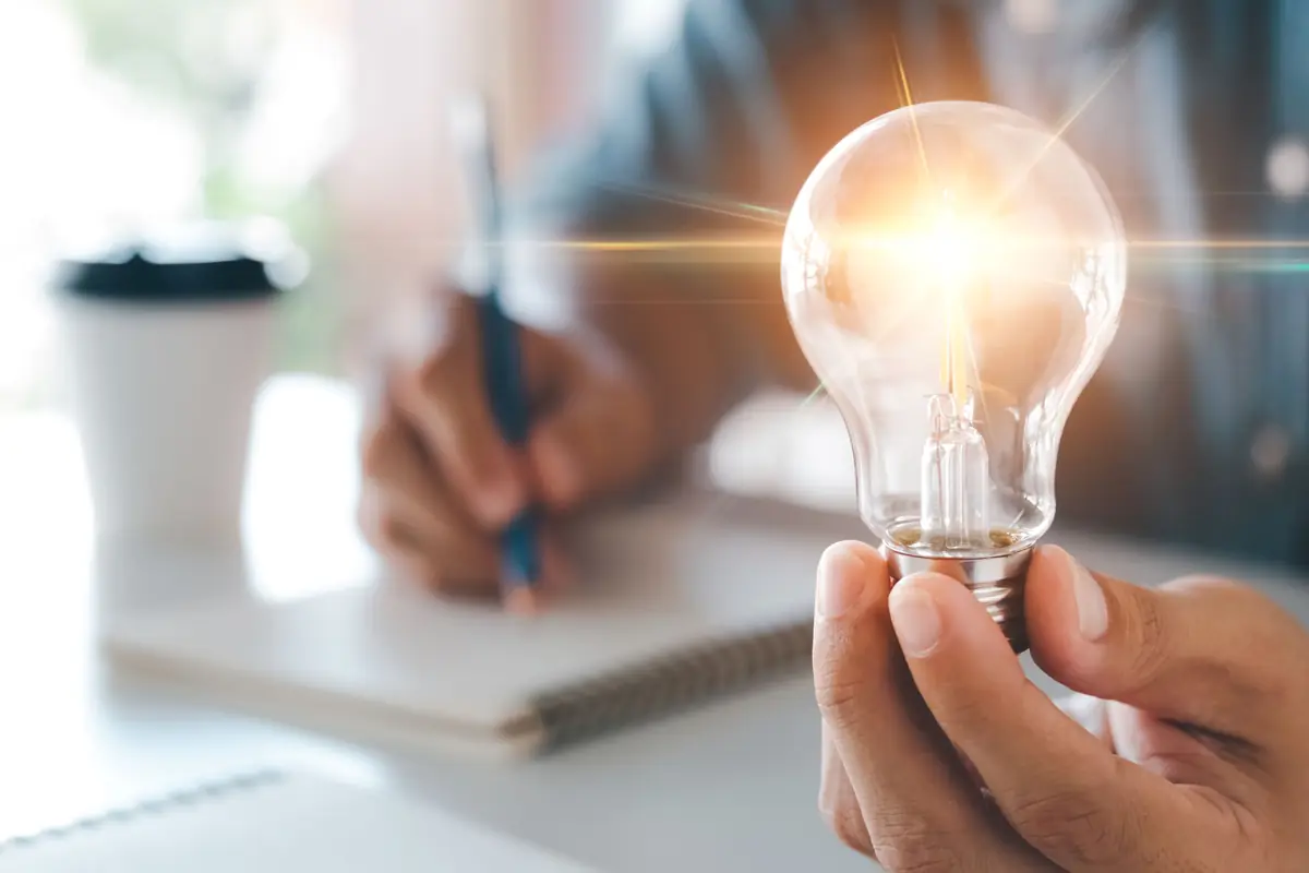 A hand holding a lit light bulb over a notebook