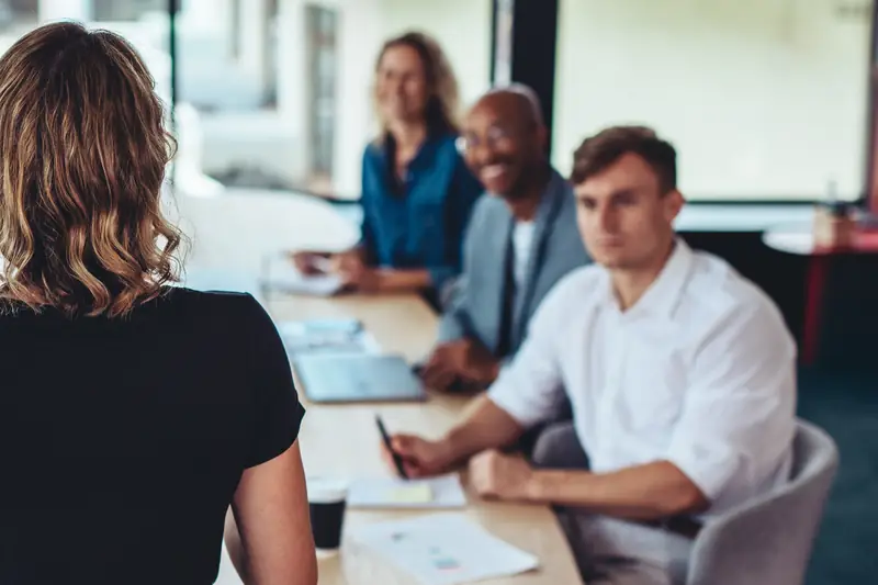 Colleagues around a meeting table listening to a speaker