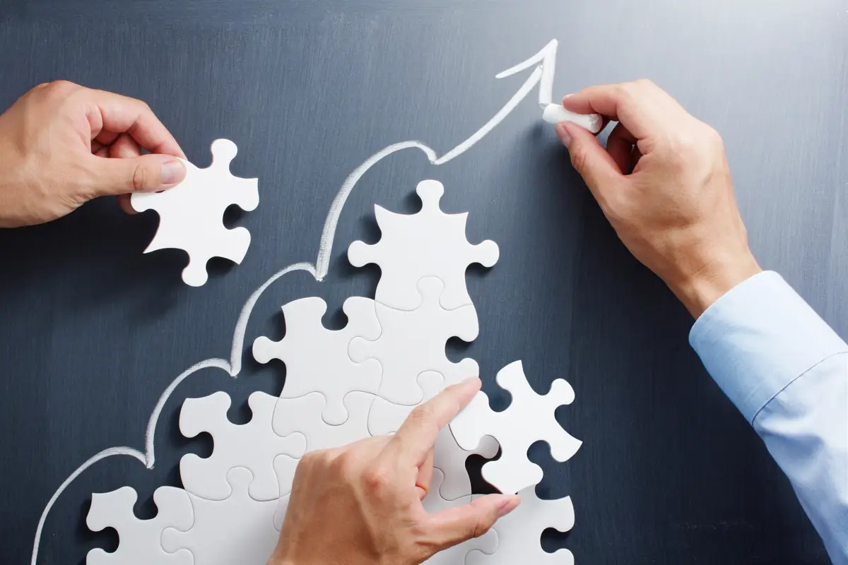 Hands placing puzzle pieces along a rising arrow