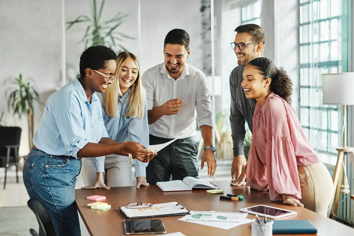 A team gathered around a table, reviewing work and smiling