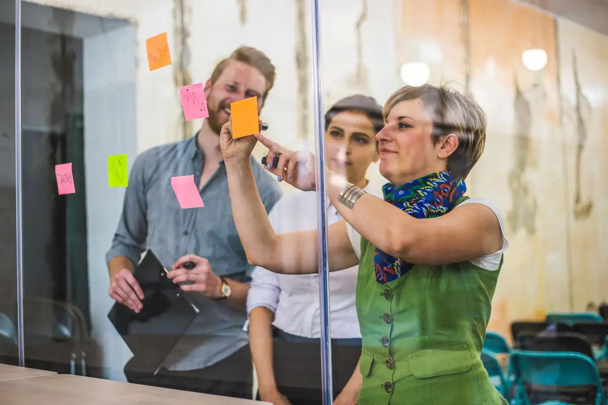A team adding sticky notes to a glass wall