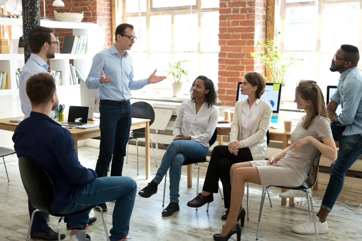 A facilitator leading a workshop with a seated group in a bright room